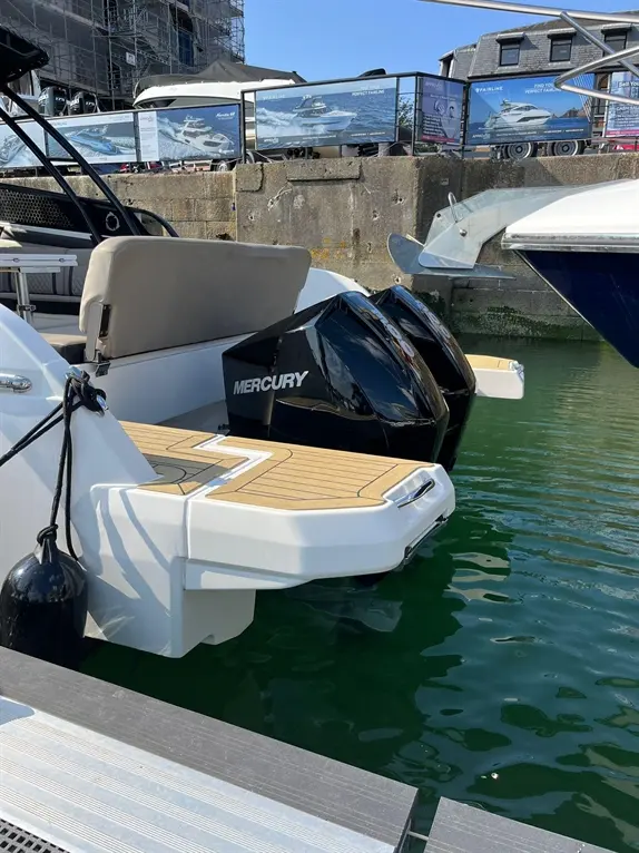 Motorboat at a marina featuring a Mercury engine, with wooden decking and nearby promotional banners for luxury boats.